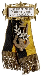 GALICJA, odznaka na agrafkę szefa podoficerskiego chóru miasta Krakowa, mosiądz złocony i emaliowany, na emalii złocony napis UNTEROFFIZIERS / SANGER - CHOR / KRAKAU, na stronie odwrotnej punca wytwórcy A.BELADA / VIEN.VII2, wstążki z materiału zakończone złotą nicią, brak szpilki od agrafki