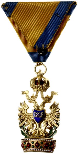 Order Żelaznej Korony, III klasa, wersja z dekoracją wojenną, nadawany od 1815/1816 do 1918, za wyjątkowe zasługi dla cesarstwa (tylko mężczyznom). Odznaczenie  w złocie próby 18 karat (0,750), waga około 23,5 g, wykonane przez znanego wiedeńskiego grawera A.E. Kochert. Sygnowane na wstążkach pod koroną austriackimi próbami złota i imiennikiem wykonawcy,,A.E. KOCHERT / VIEN A.E, wstążka z dekoracją wojenną w formie dwóch skrzyżowanych złotych mieczy. Całość w oryginalnym etui z epoki. Odznaczenia wykonane w złocie bardzo rzadko występują na rynku. Katalog odznaczeń austriackich. A. Marko pozycja nr 074c.