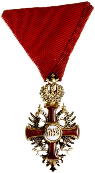 Order Franciszka Józefa, Krzyż Kawalerski, wykonany w złocie próby 18 karat (0,750), waga 12,68 grama, wersja bez dekoracji wojennych, wybity przez wiedeńskiego grawera, sygnowany na ogniwie łączącym austriackimi próbami złota i wykonawcy,V.Mayer´s Söhne in Wien” całość w oryginalnym etui firmy V.Mayer´s Söhne in Wien z data 1898. Order został ustanowiony 2 grudnia 1849 przez dziewiętnastoletniego wówczas cesarza Austrii i króla Węgier Franciszka Józefa I w pierwszą rocznicę objęcia przez niego tronu. Insygnia orderu to oznaka i gwiazda dla I i II klasy. Wąski krzyż typu kawalerskiego, emaliowany na czerwono ze złotym obramowaniem. Medalion awersu, emaliowany na biało, zawierał w środku złoty monogram założyciela “FJ”. Medalion rewersu ukazywał datę “1849”. Krzyż orderowy położony był na złotym dwugłowym, podwójnie ukoronowanym, częściowo emaliowanym na czarno orle monarchii habsburskiej, noszącym w dziobach złoty łańcuch, na dolnej części którego widniała dewiza panowania Franciszka Józefa, “Viribus unitis” (“Zjednoczonymi siłami”). Katalog odznaczeń austriackich. A. Marko pozycja nr 098c.
