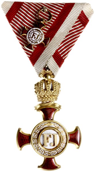 Złoty krzyż zasługi z koroną dla cywili -Zivil-Verdienstkreuz. Wykonany w złocie próby 18 karat (0750), waga 15,95 grama przez firmę wiedeńską “V.MAYER´s SÖHNE,sygnowany na ogniwie łączącym austriackimi próbami złota i wykonawcy, całość w oryginalnym etui tej firmy z datą 1905. Krzyż zasługi obywatelskiej został zatwierdzony przez cesarza Franciszka Józefa I dniu 16 lutego 1850 r. Oznaką odznaczenia jest krzyż z czerwonymi emaliowanymi ramionami krzyżowymi, rozszerzającymi się ku zewnętrznym i zaokrąglonym końcom. Z przodu znajdują się inicjały cesarza Franciszka Józefa - FJ  - na białej emaliowanej tarczy, okrągłej VIRIBUS UNITIS. Z drugiej strony jest rok 1849. Na wstążce jest miniatura odznaczenia wykonana w złocie, wariant bez korony. Katalog odznaczeń austriackich A. Marko pozycja nr 138c.