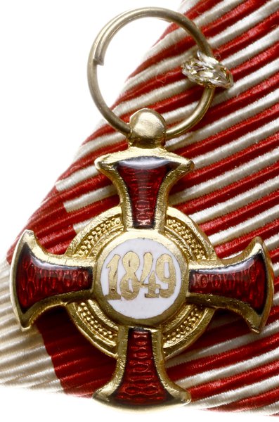 Złoty krzyż zasługi z koroną dla cywili -Zivil-Verdienstkreuz. Wykonany w złocie próby 18 karat (0750), waga 15,95 grama przez firmę wiedeńską “V.MAYER´s SÖHNE,sygnowany na ogniwie łączącym austriackimi próbami złota i wykonawcy, całość w oryginalnym etui tej firmy z datą 1905. Krzyż zasługi obywatelskiej został zatwierdzony przez cesarza Franciszka Józefa I dniu 16 lutego 1850 r. Oznaką odznaczenia jest krzyż z czerwonymi emaliowanymi ramionami krzyżowymi, rozszerzającymi się ku zewnętrznym i zaokrąglonym końcom. Z przodu znajdują się inicjały cesarza Franciszka Józefa - FJ  - na białej emaliowanej tarczy, okrągłej VIRIBUS UNITIS. Z drugiej strony jest rok 1849. Na wstążce jest miniatura odznaczenia wykonana w złocie, wariant bez korony. Katalog odznaczeń austriackich A. Marko pozycja nr 138c.